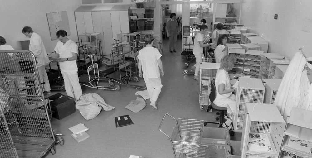 Gävle sjukhus transportavdelning den 5 maj 1989, fotograf är sjukhusfotografen Sven Östberg. I bild ser vi det organiserade kaoset när dagens post och paket ska transporteras ut till avdelningarna. Postsortering pågår vid postborden till höger, till vänster står sparkcyklarna redo att fyllas och i postfacken närmast i bild kan vi se, om vi tittar noga, att konstföreningens reklamblad är på väg att hitta ut till sina medlemmar.