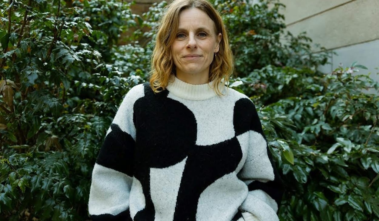 Person ståendes framför en grön buske iklädd en svart och vit mönstrad tröja.