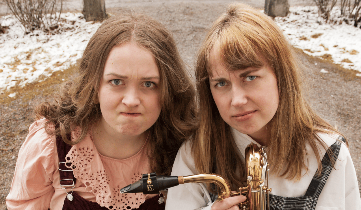 Två kvinnor står bredvid varandra och håller i en saxofon.