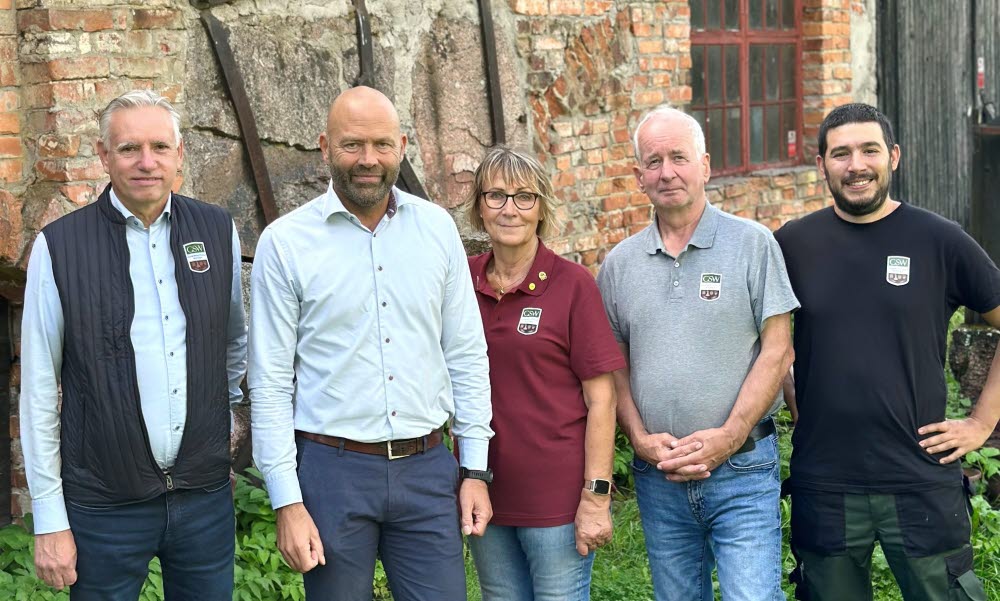 Fem personer står i helkroppsfigur framför en gammal tegelbyggnad.