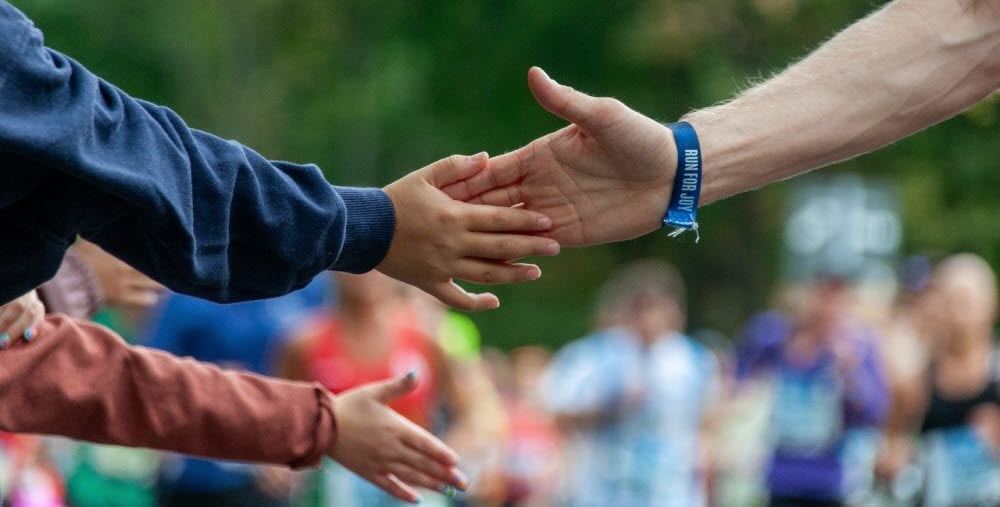 Händer som möts. I bakgrunden syns färgklädda människor.